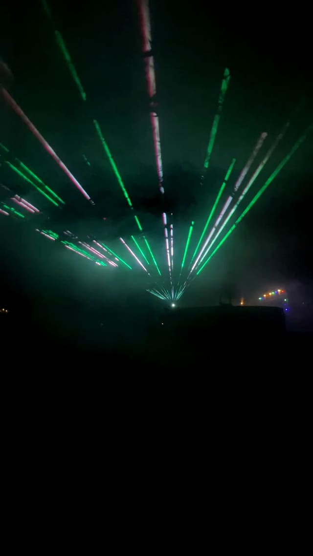 Groene en witte laserwaaier boven een donker feestterrein