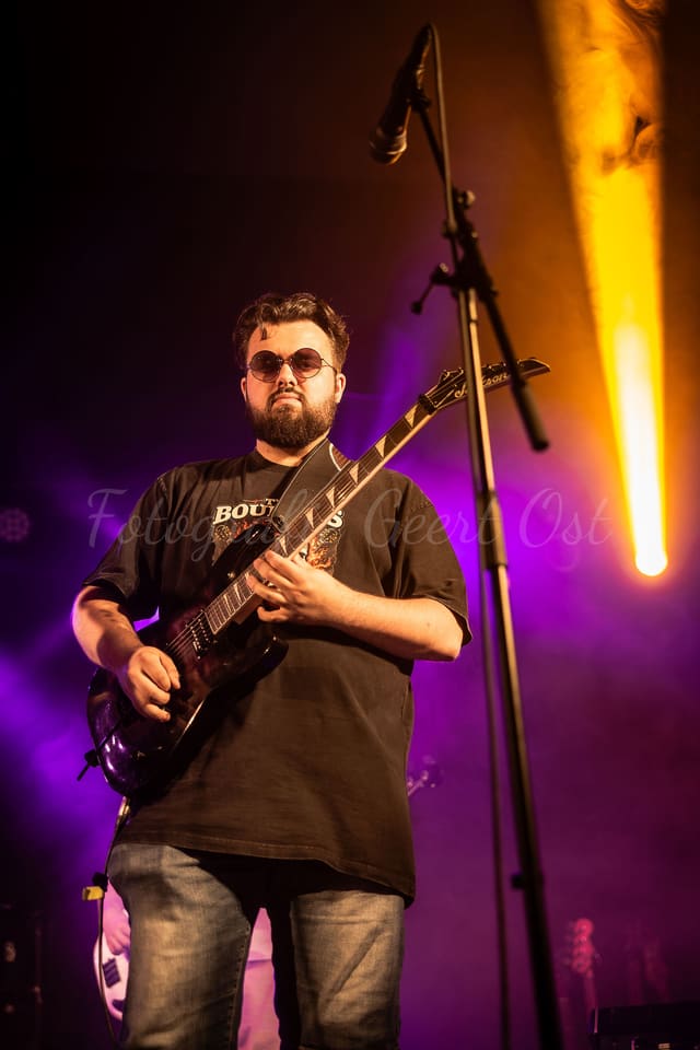 Gitarist op het podium in paars licht met een warme amberkleurige straal ernaast