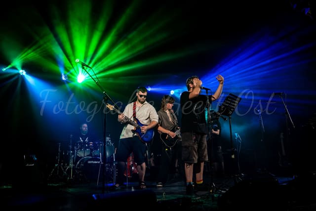 Band op een donker podium met groene en blauwe beams die uitwaaieren