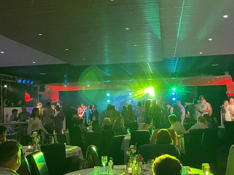 Feestzaal in groen en blauw licht met mensen rond statafels